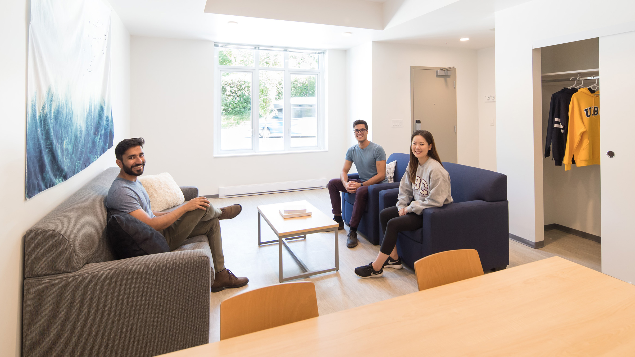 Three smiling students sit in the living room area of a residence room.